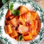 Paccheri pasta in tomato sauce in a green and white patterned bowl sitting on a wooden surface.
