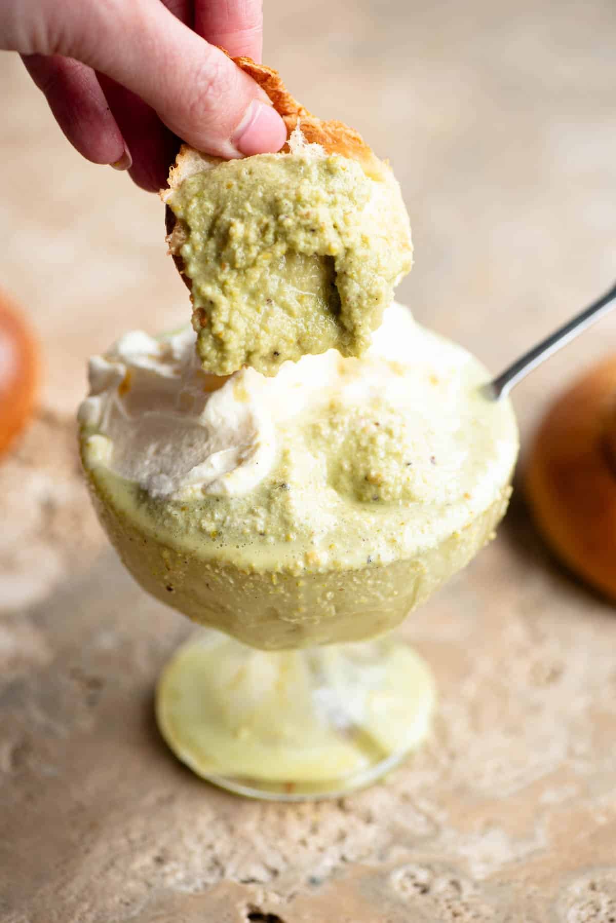 A piece of brioche being dunked into pistachio granita.