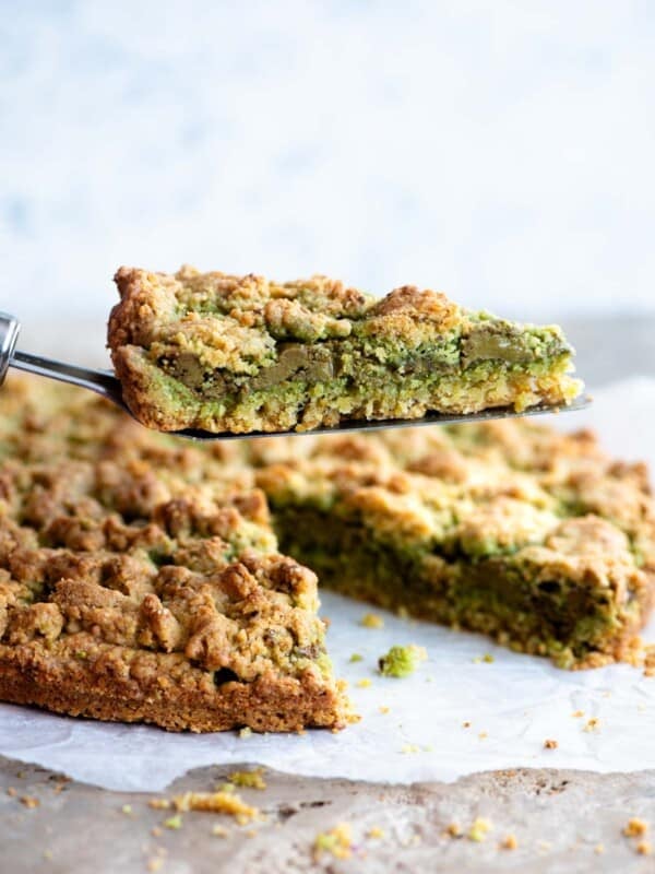A cake slice holding up a slice of pistachio crumb cake showing a layer of pistachio in the middle.