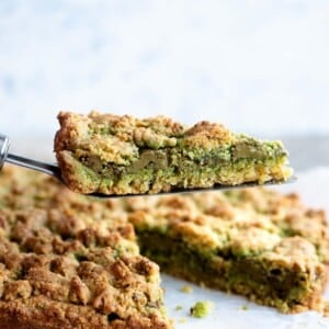 A close cup of a slice of pistachio crumb cake being help up on a cake server.