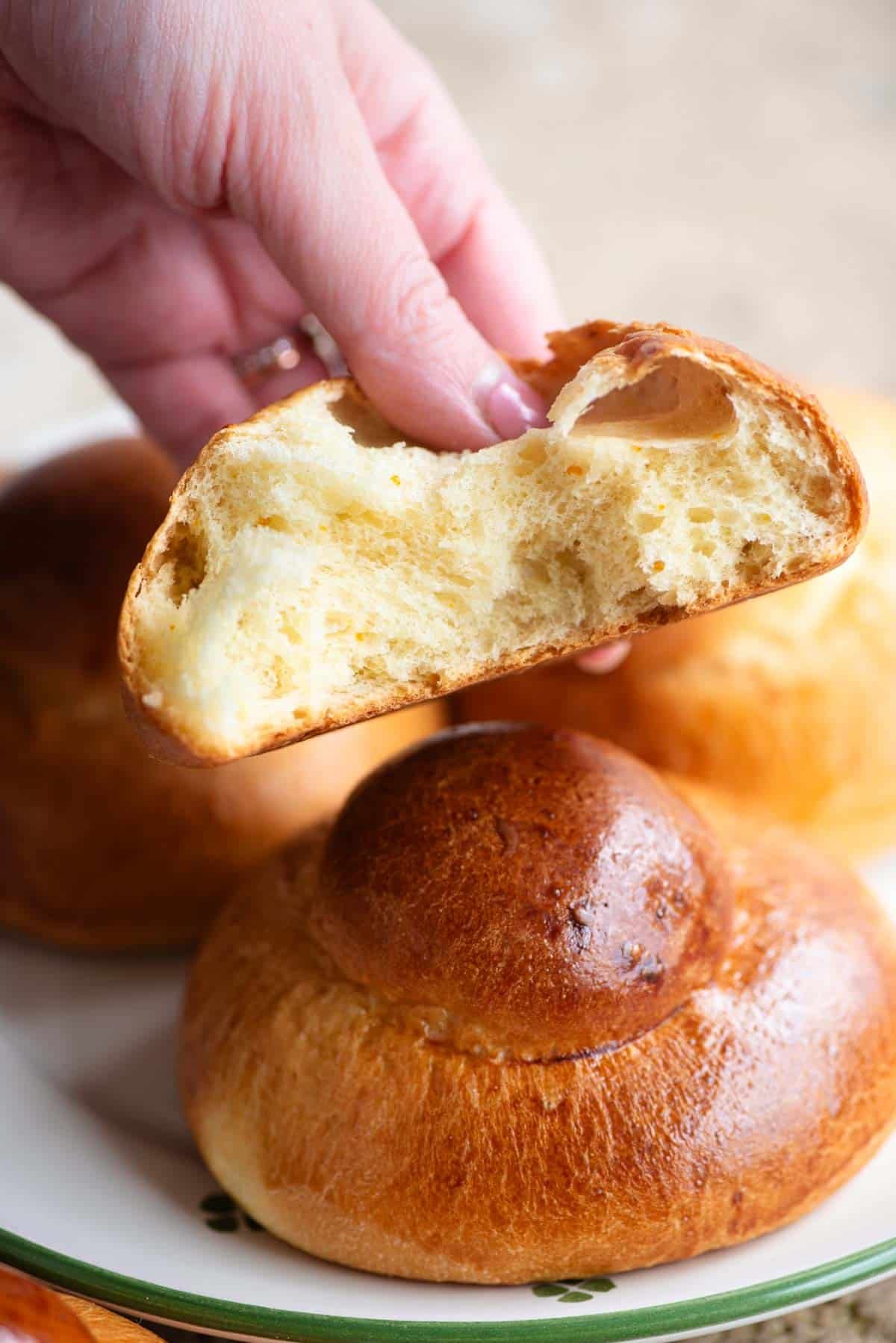 A hand holding a Sicilian brioche bun cut in half showing the airy interior.