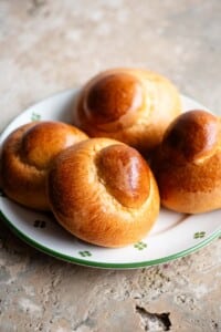 Four Sicilian brioche buns on a plate sitting on a travertine surface.