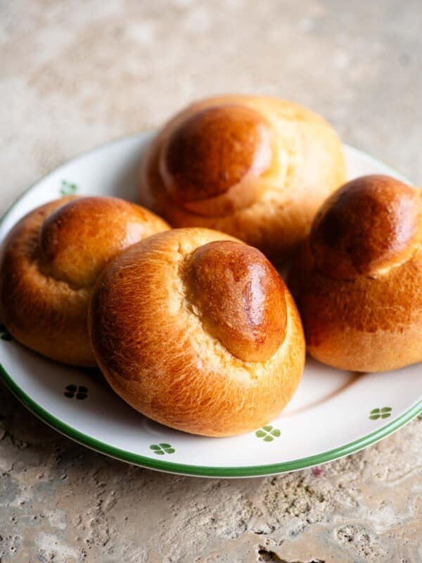 Four Sicilian brioche buns on a plate sitting on a travertine surface.