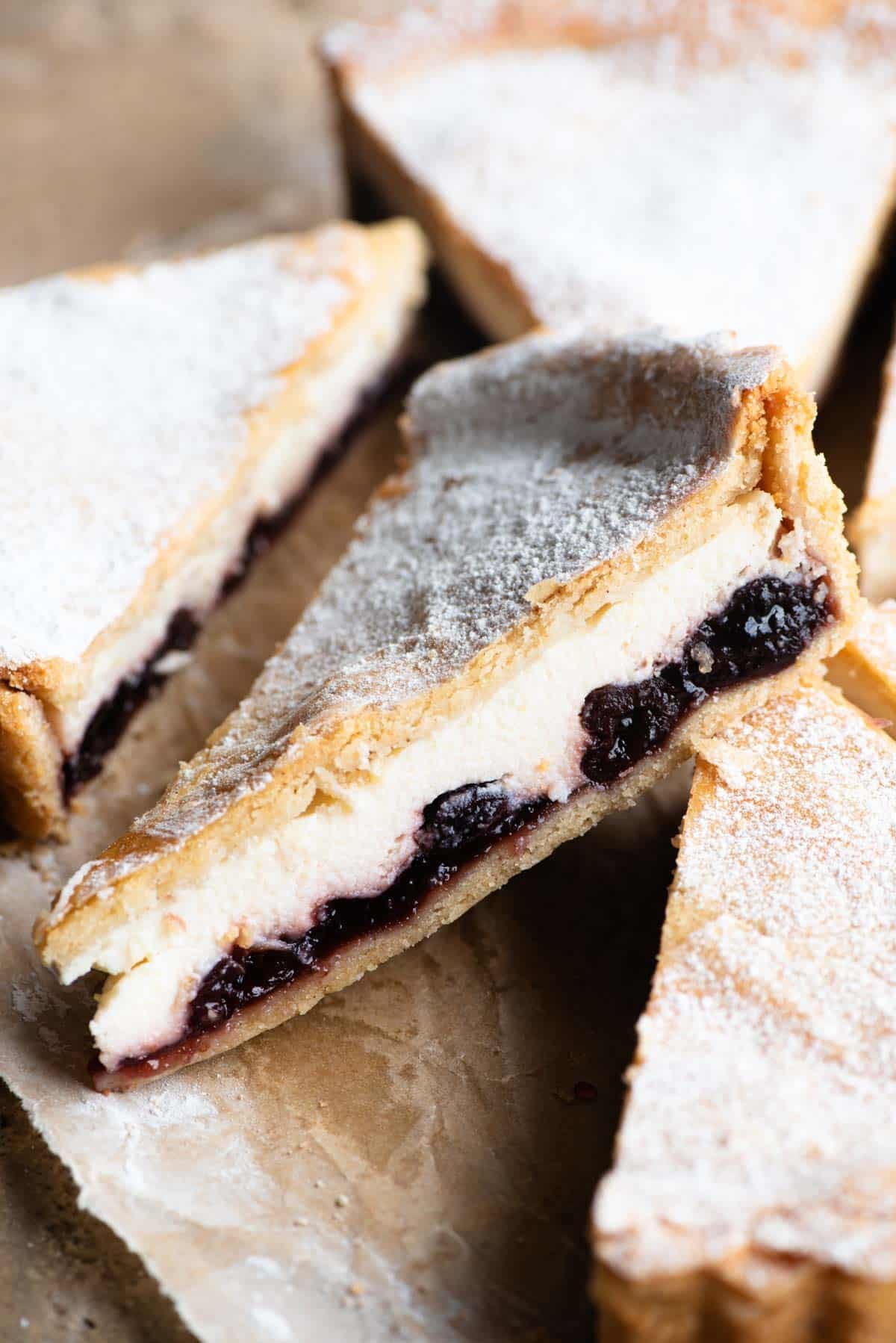 A close up of a slice of ricotta and cherry crostata dusted with powdered sugar.