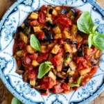 A close up of fried eggplant in a cherry tomato and basil sauce. It's presented in a blue and white country style bowl.