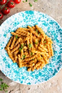 Pasta in a tuna tomato sauce in a blue and white spotted plate sitting on a travertine surface.