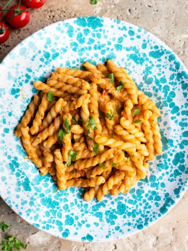 Pasta in a tuna tomato sauce in a blue and white spotted plate sitting on a travertine surface.
