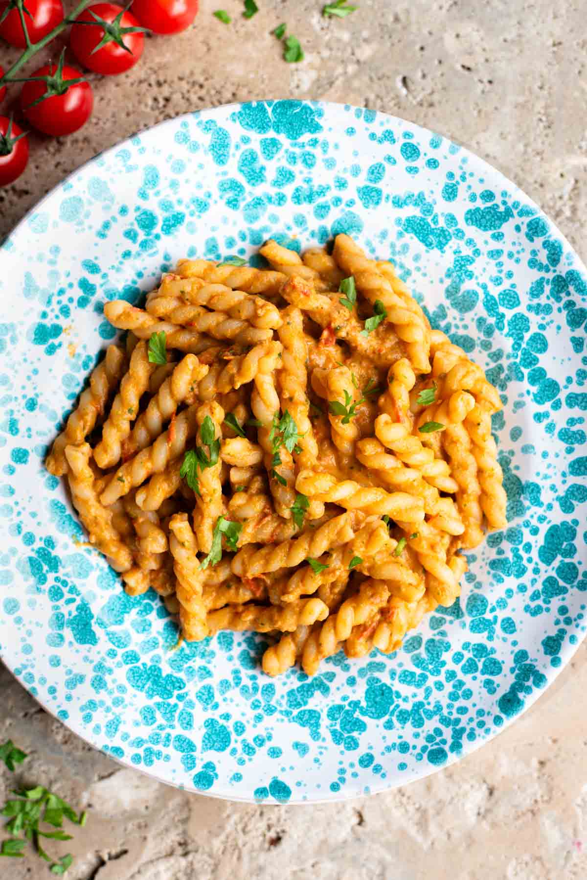 Pasta in a tuna tomato sauce in a blue and white spotted plate sitting on a travertine surface.