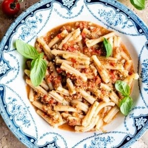 A cropped square image of pasta in tomato sauce in a blue and white vintage style bowl.