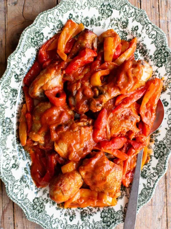 Italian chicken and peppers in a tomato sauce on a large platter serving plate on a rustic wooden surface.