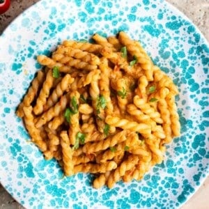 A cropped close up of tuna pasta sauce with gemelli pasta in a blue and white speckled bowl.