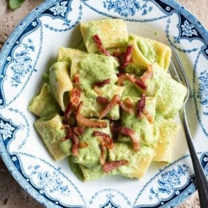 A close up of a creamy zucchini pasta topped with crispy pancetta.