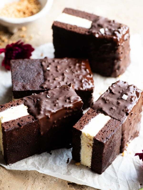 Four chocolate ice cream sandwiches with vanilla ice cream in the middle and dipped in chocolate and hazelnuts on a travertine surface.