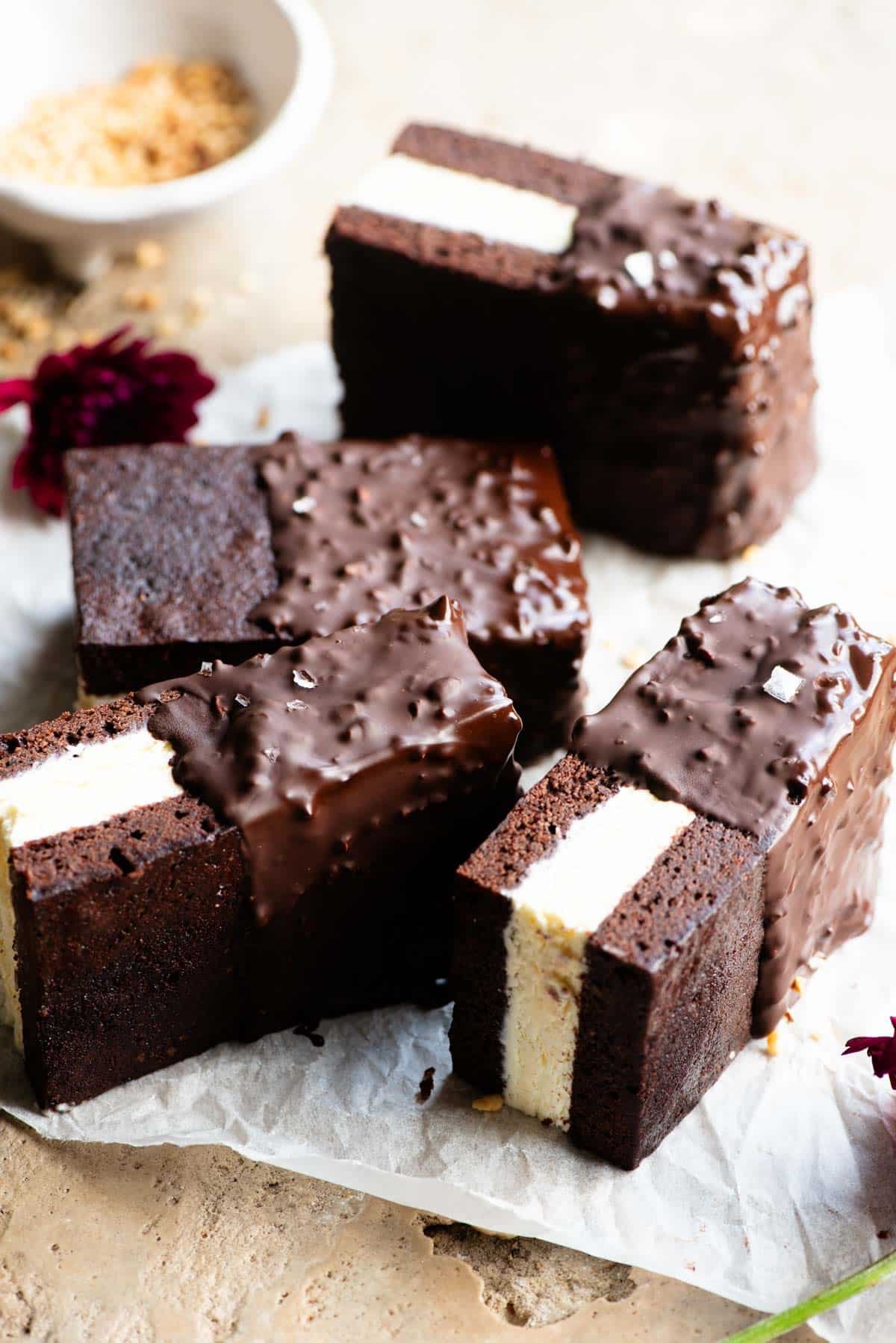 Four chocolate ice cream sandwiches with vanilla ice cream in the middle and dipped in chocolate and hazelnuts on a travertine surface.