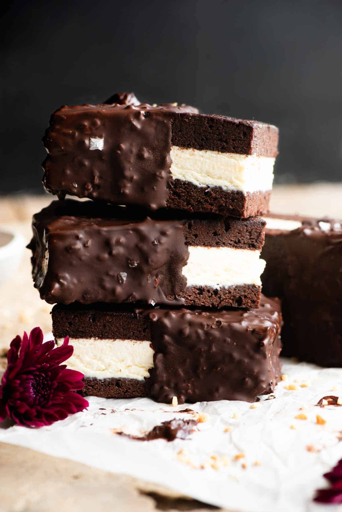 Three chocolate and vanilla ice cream sandwiches stacked on top of each other the surface is travertine and the background is black.