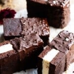 Four chocolate ice cream sandwiches with vanilla ice cream in the middle and dipped in chocolate and hazelnuts on a travertine surface.