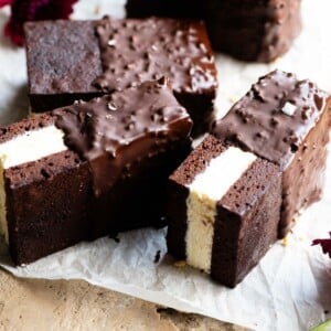 Three ice cream sandwiches with a chocolate sponge and vanilla ice cream sitting on their sides on some baking parchment.