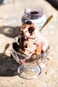 An Italian ice cream sundae in a glass bowl with cream and cherries on top sitting on a travertine surface.
