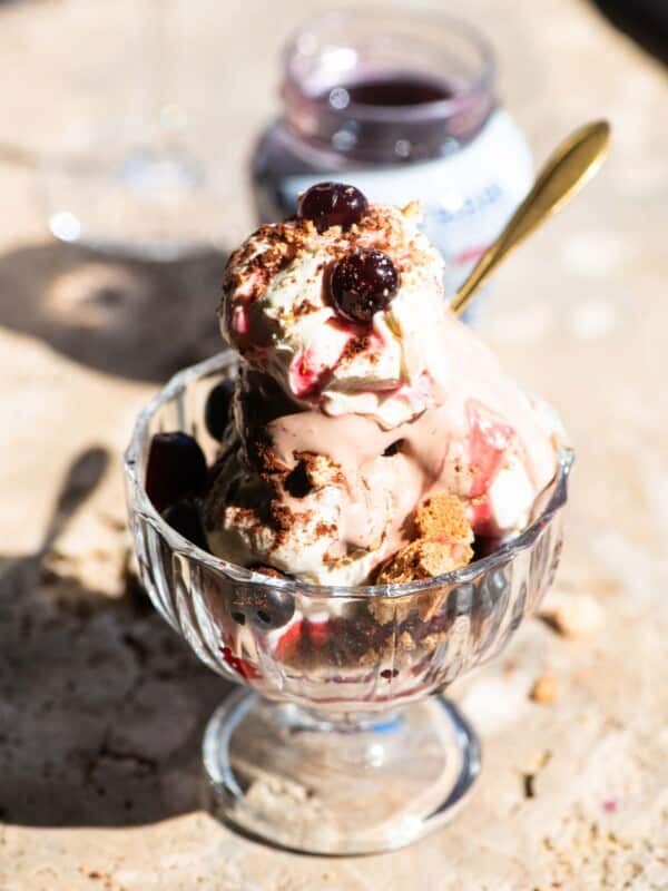 An Italian ice cream sundae in a glass bowl with cream and cherries on top sitting on a travertine surface.