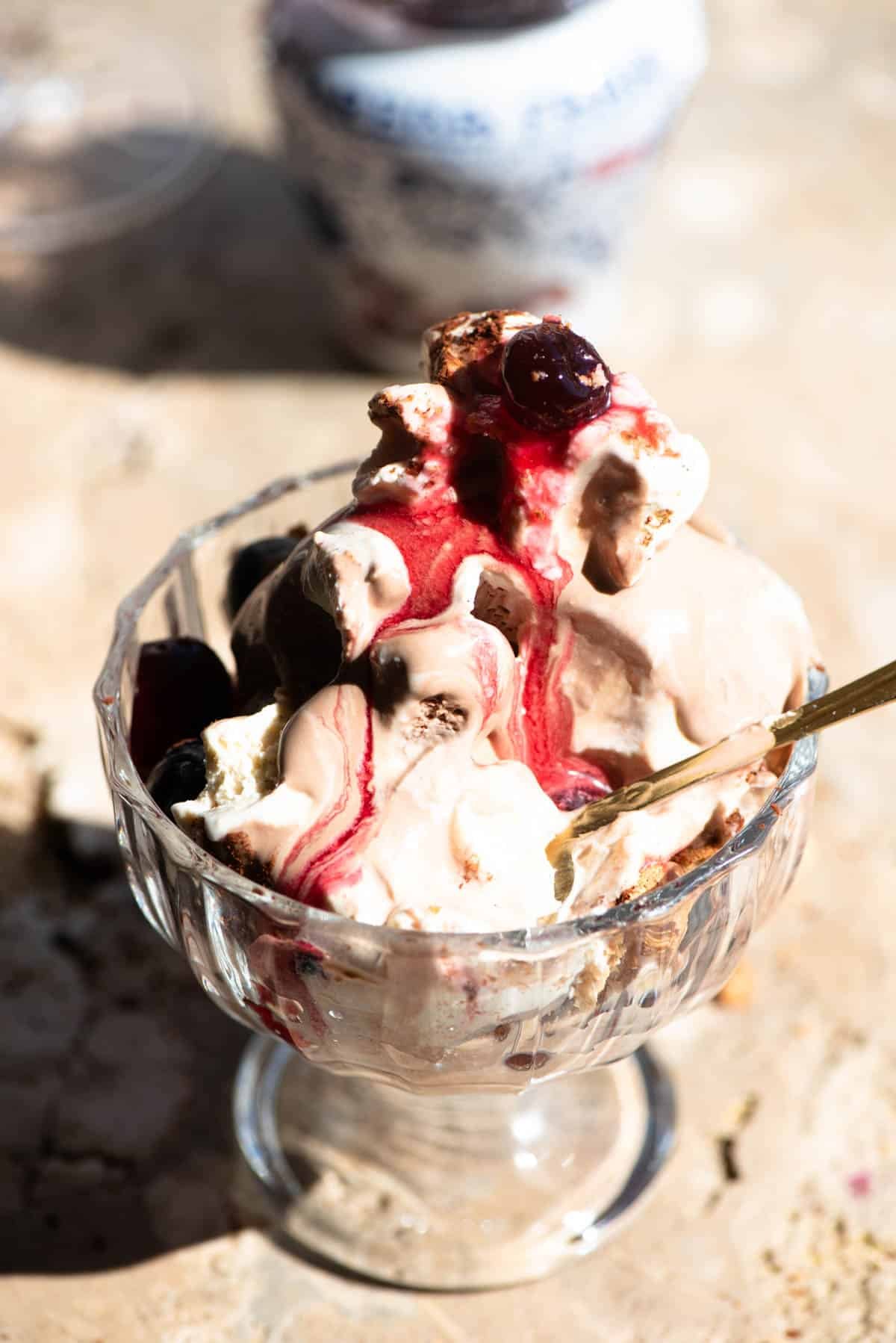 A close up of an Italian ice cream sundae melting in a glass bowl with a amarena cherries.