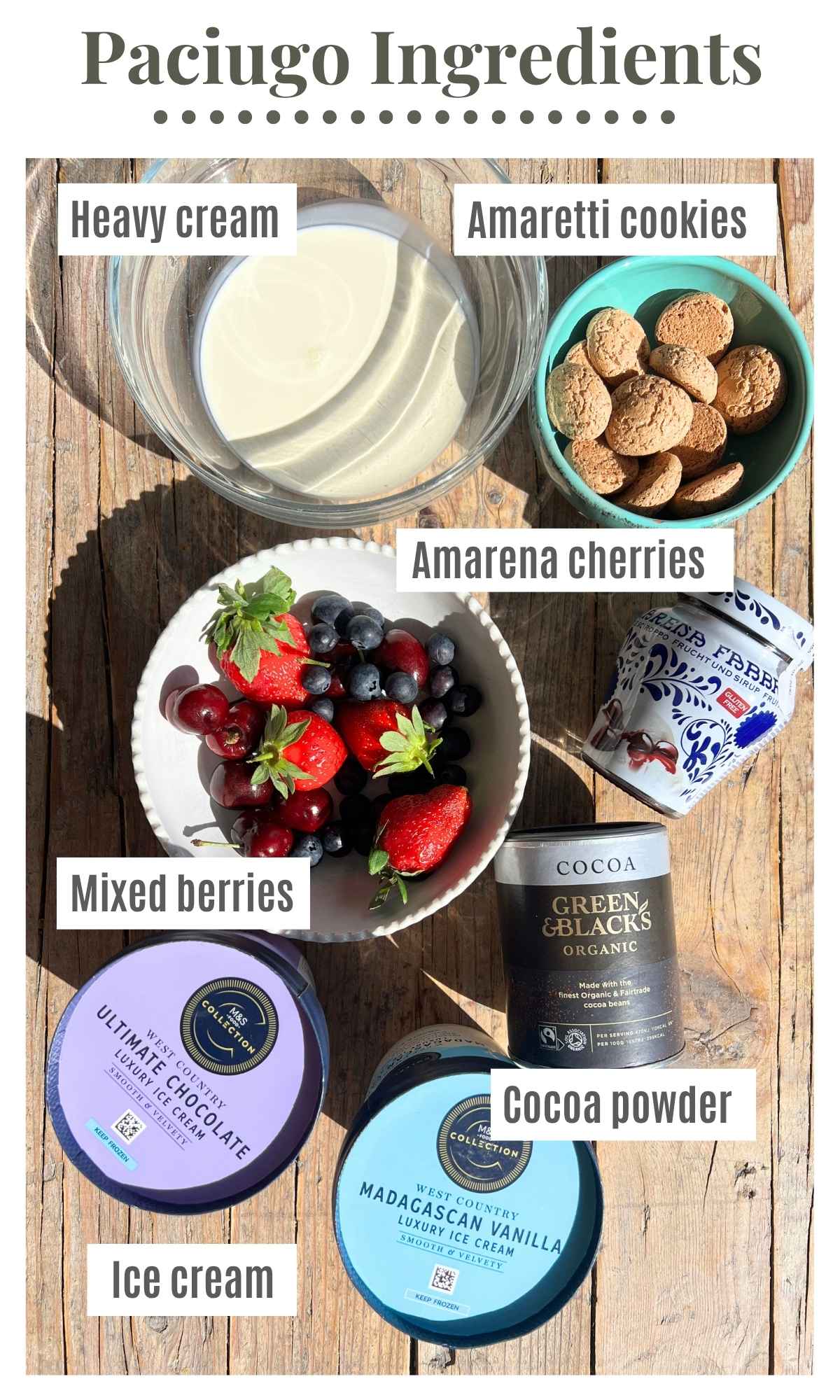 All the ingredients to make an Italian ice cream sundae laying on a rustic wooden surface; mixed berries, amarena cherries, heavy cream, ice cream, cocoa powder and amaretti cookies.