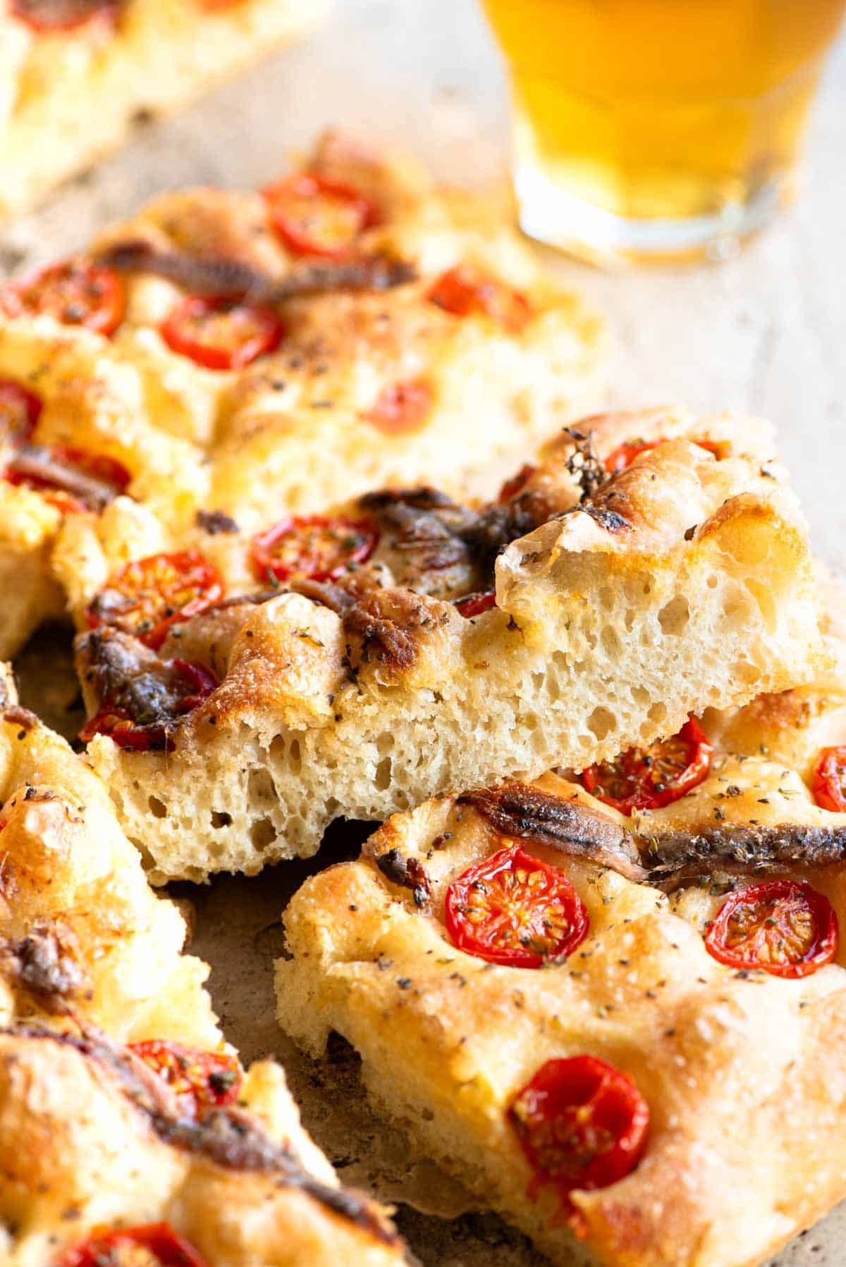 A close up of a slice of tomato and anchovy focaccia on it's side showing the airy and bubbly texture inside.
