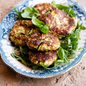 A cropped image of zucchini patties on a blue and white serving plate.