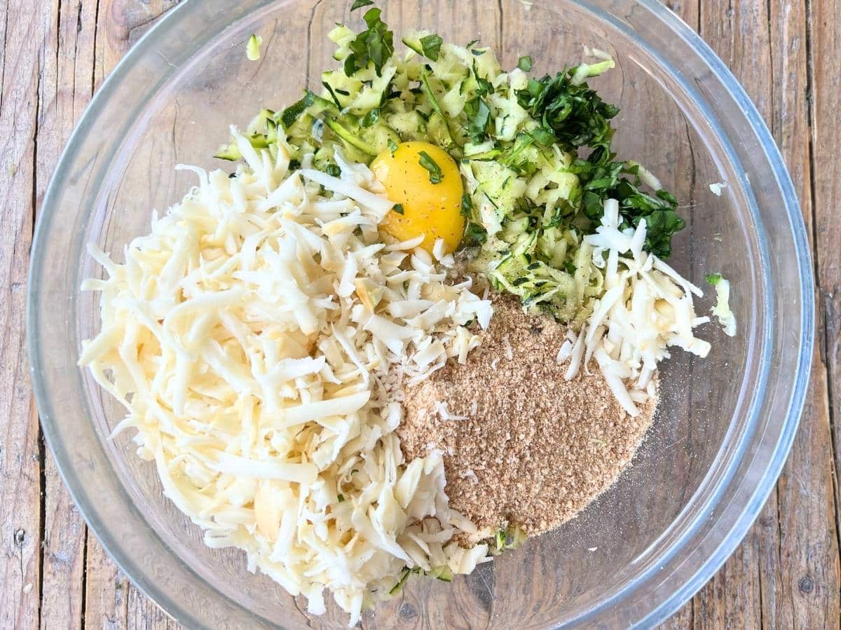 Egg, zucchini, breadcrumbs, cheese, nutmeg, garlic and basil in a mixing bowl.