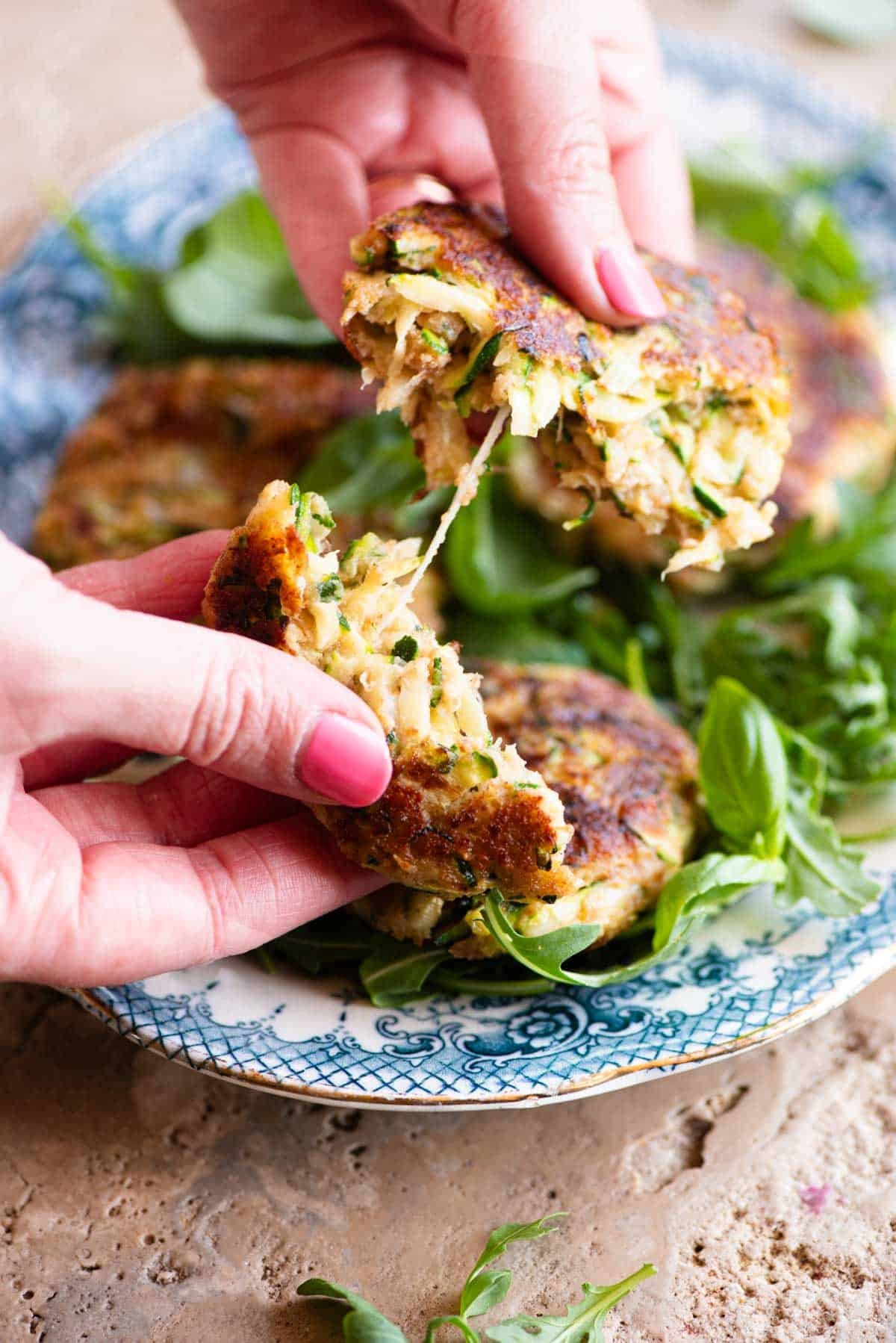 Two hands pulling a zucchini patty in half with cheese pulling in the middle.