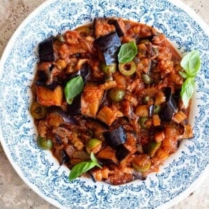 A close up of Sicilian eggplant caponata in a blue and white bowl with basil on top.
