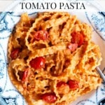 Creamy sun dried tomato pasta in a blue and white bowl sitting on a travertine surface. The text overlay reads: Creamy Sun-Dried Tomato Pasta.