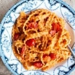 Ribbons of mafaldine pasta in a blue and white vintage style bowl sitting on a travertine surface with cherry tomatoes on the vine at the side.