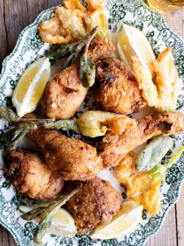 Italian fried chicken on a serving platter with fried zucchini blossoms and sage.