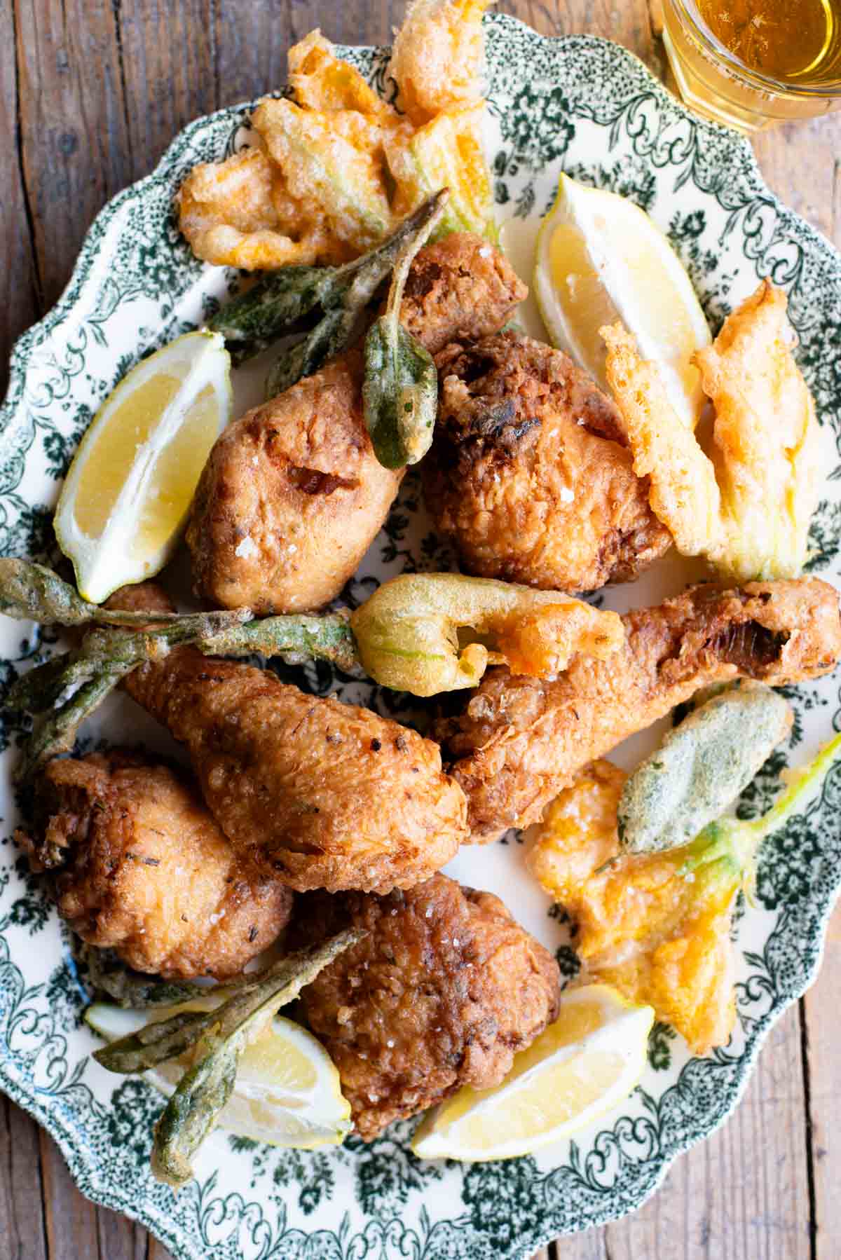 Italian fried chicken on a serving platter with fried zucchini blossoms and sage.