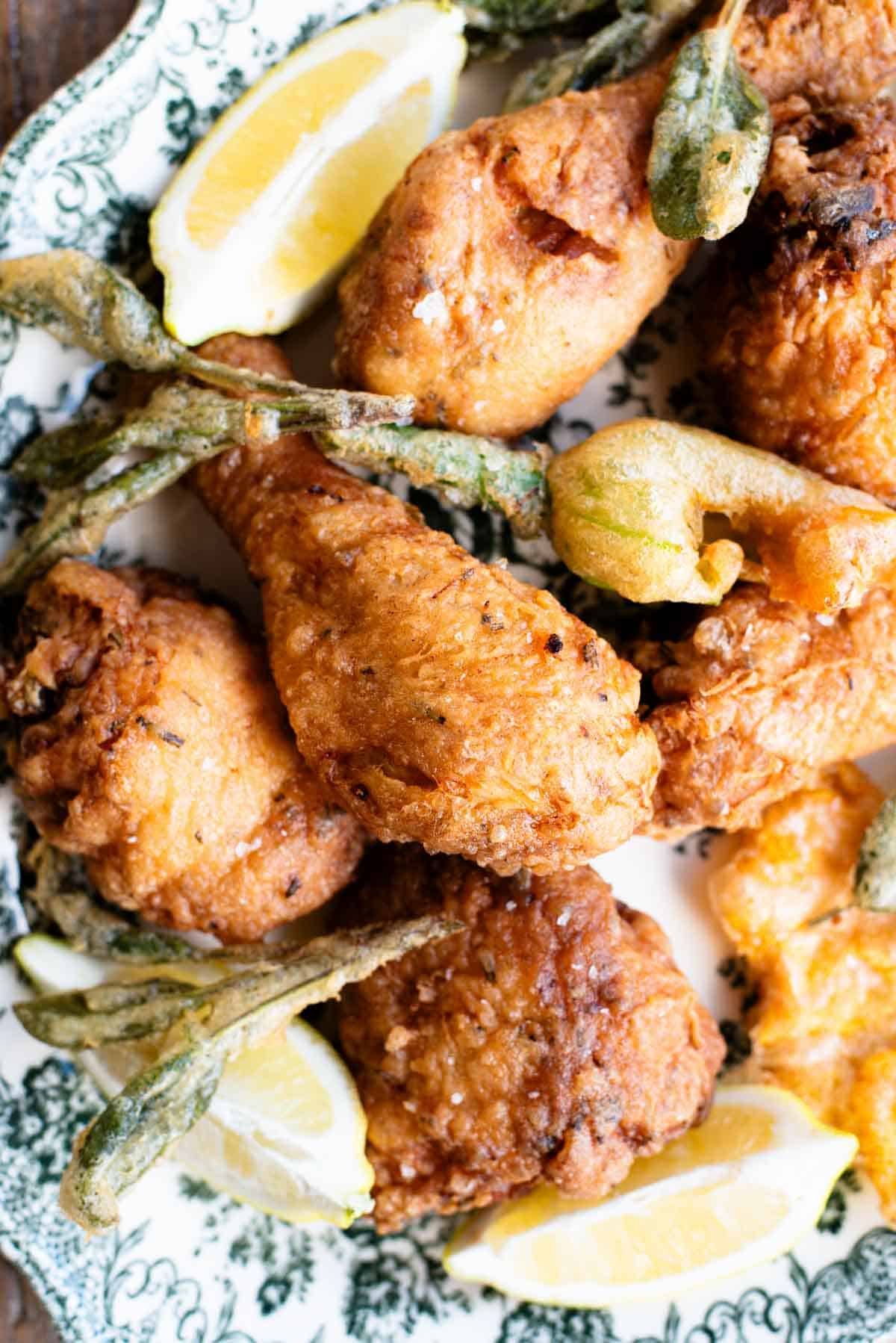 A close up of Italian fried chicken on a serving platter with sage leaves and zucchini blossoms.