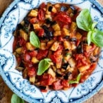 Fried eggplant in tomato sauce in a blue and white vintage bowl sitting on a wooden surface.