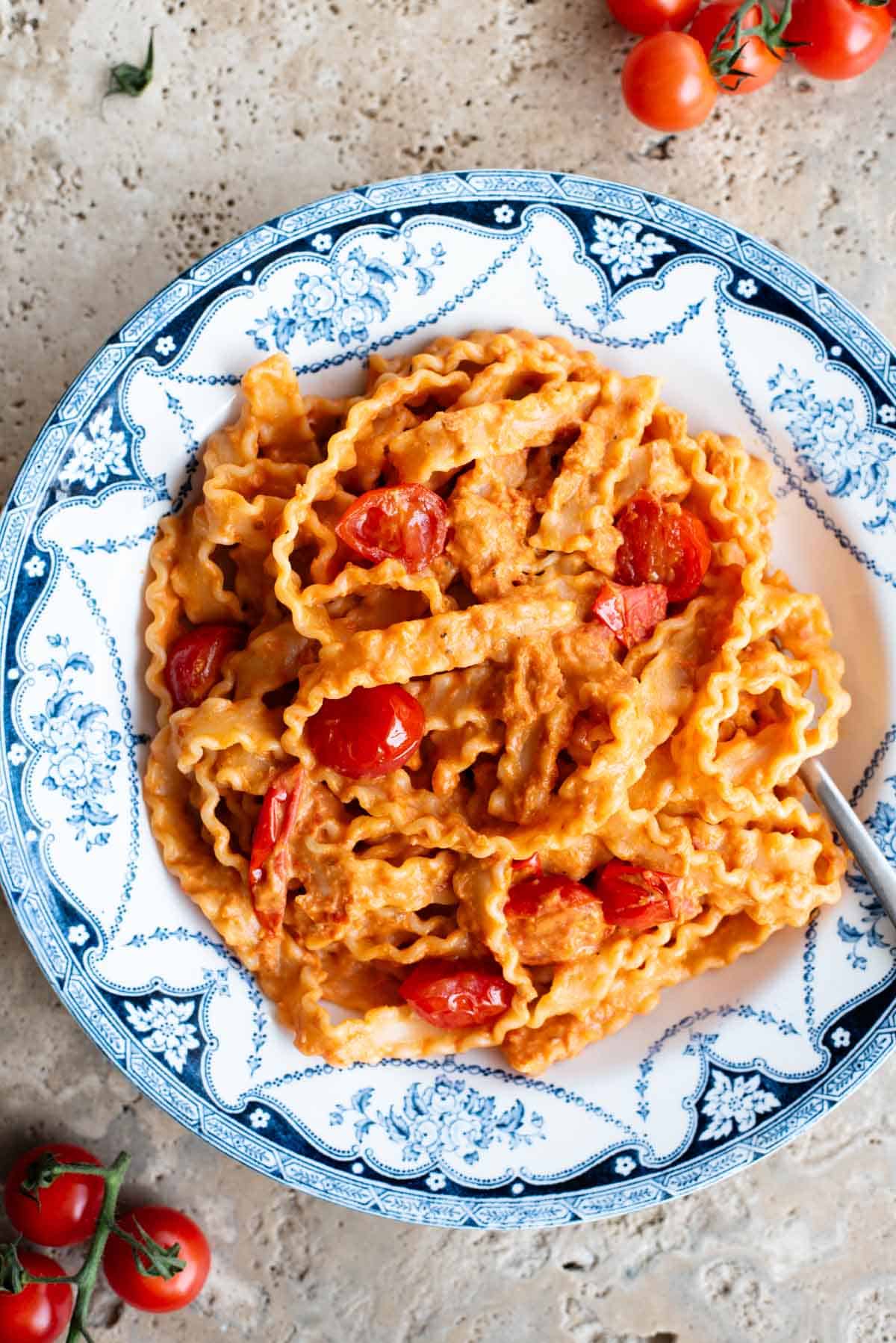 Pasta ribbons in a creamy tomato sauce in a blue and white vintage style bowl with sauteed cherry tomatoes on top.