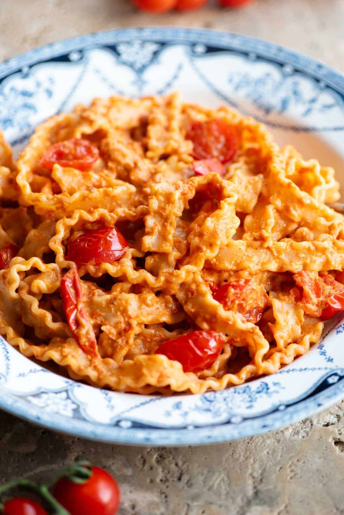 A close up of pasta ribbons in a tomato and stracchino cheese sauce on a blue and white vintage style bowl.