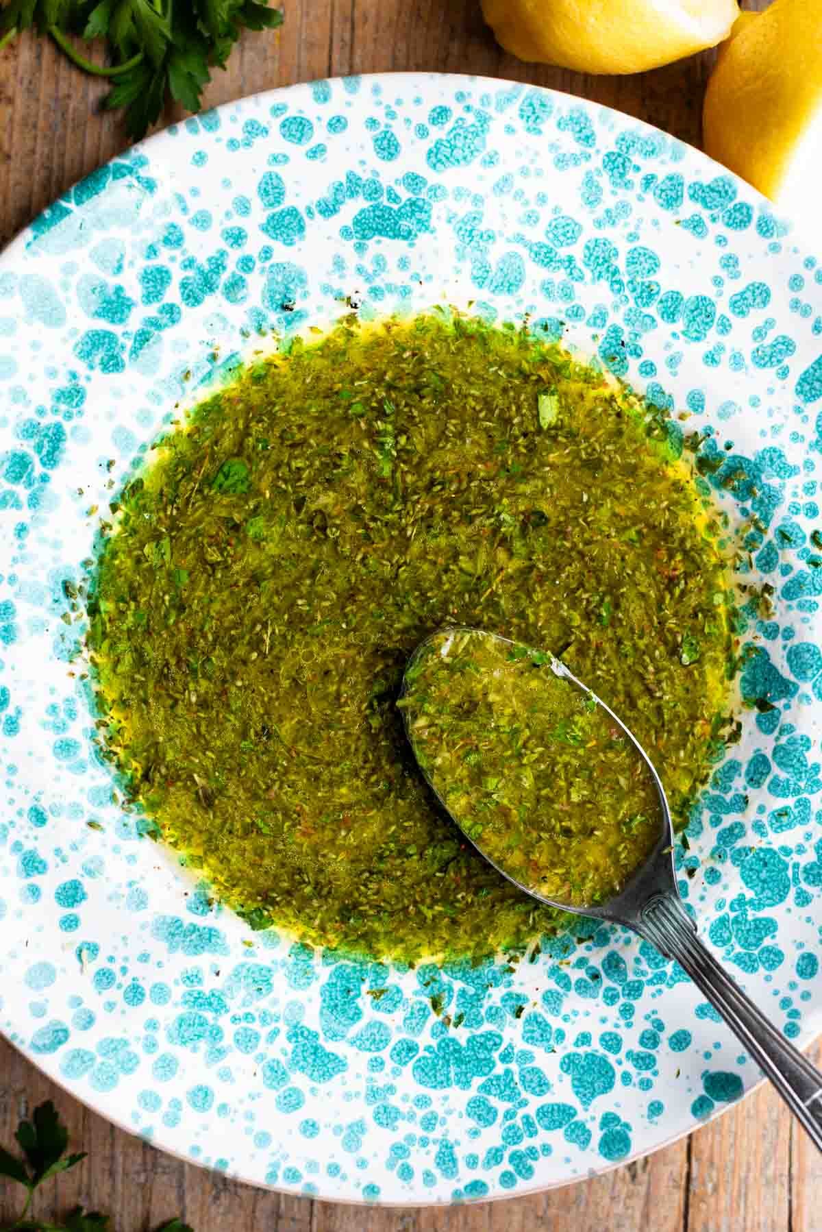 Salmoriglio sauce in a green splatter pattern bowl with a spoon.
