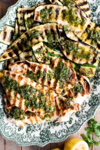 Grilled chicken and vegetables on a platter with Salmoriglio sauce over the top.