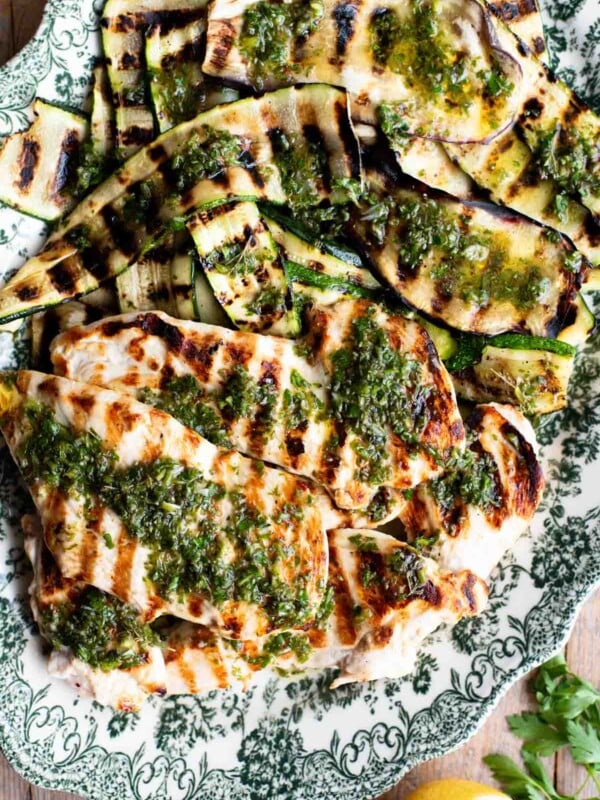 Grilled chicken and vegetables on a platter with Salmoriglio sauce over the top.