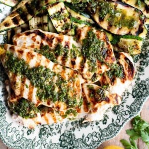 A close up of grilled chicken and veg on a plate topped with Salmoriglio herb sauce.