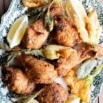 A green and white platting on a rustic wooden surface with Italian fried chicken, zucchini blossoms and sage leaves.