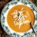 Roasted vegetable soup in a green and white vintage style bowl topped with grated cheese and thyme.