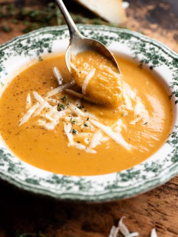 A close up of a spoon scooping up some roasted vegetable soup from a vintage style bowl.