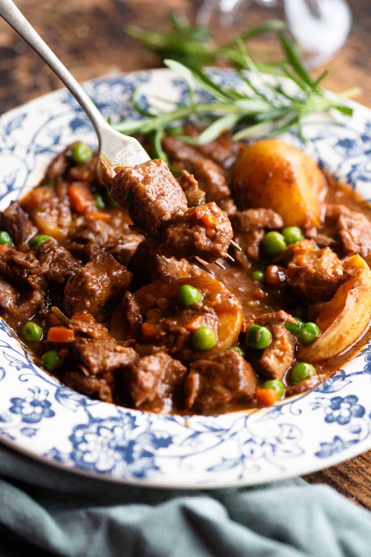 A close up of a fork picking up some beef from a bowl of beef stew.