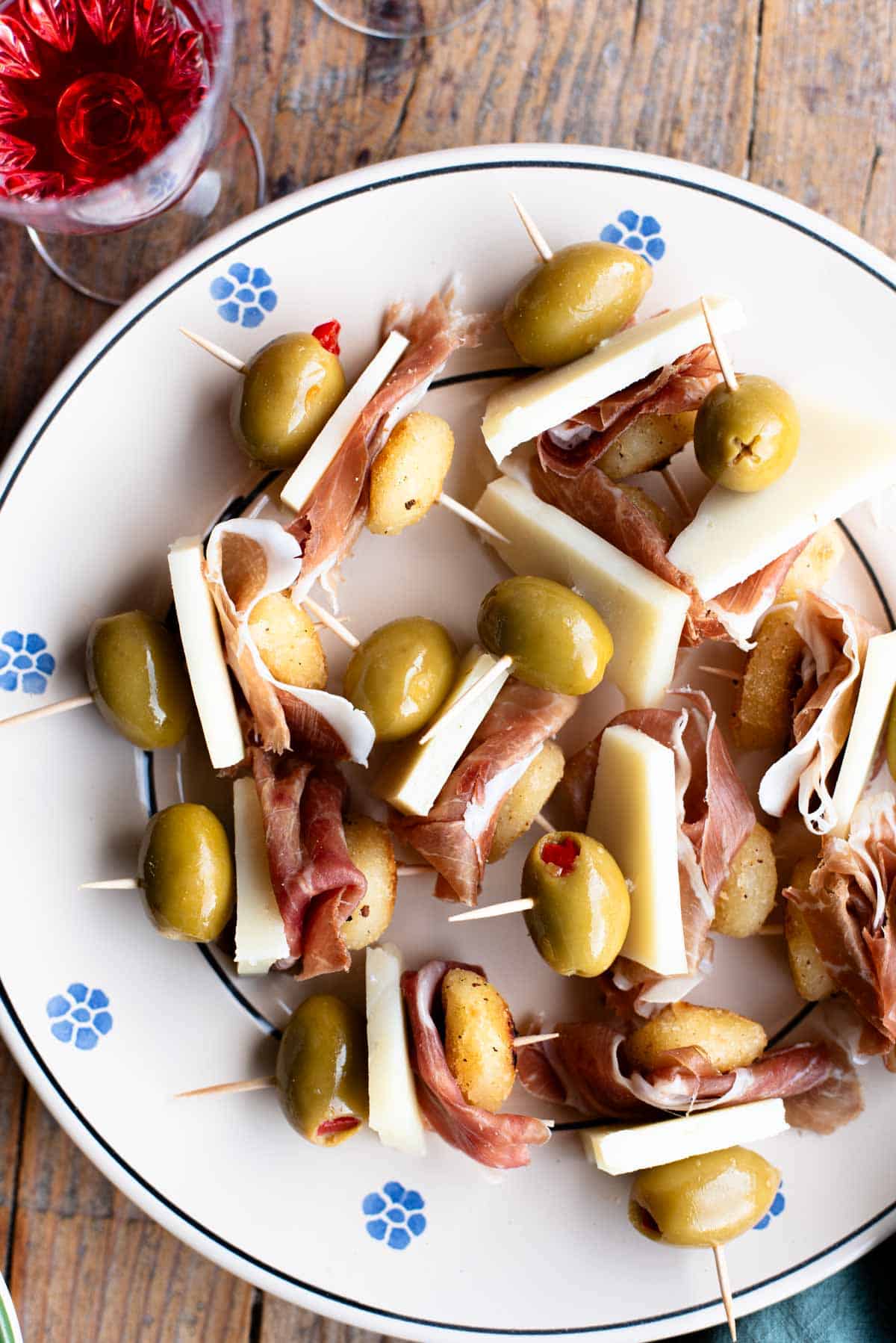 Little fried gnocchi appetizers with prosciutto, pecorino and olives in toothpicks sitting on a plate with a rustic wooden background.