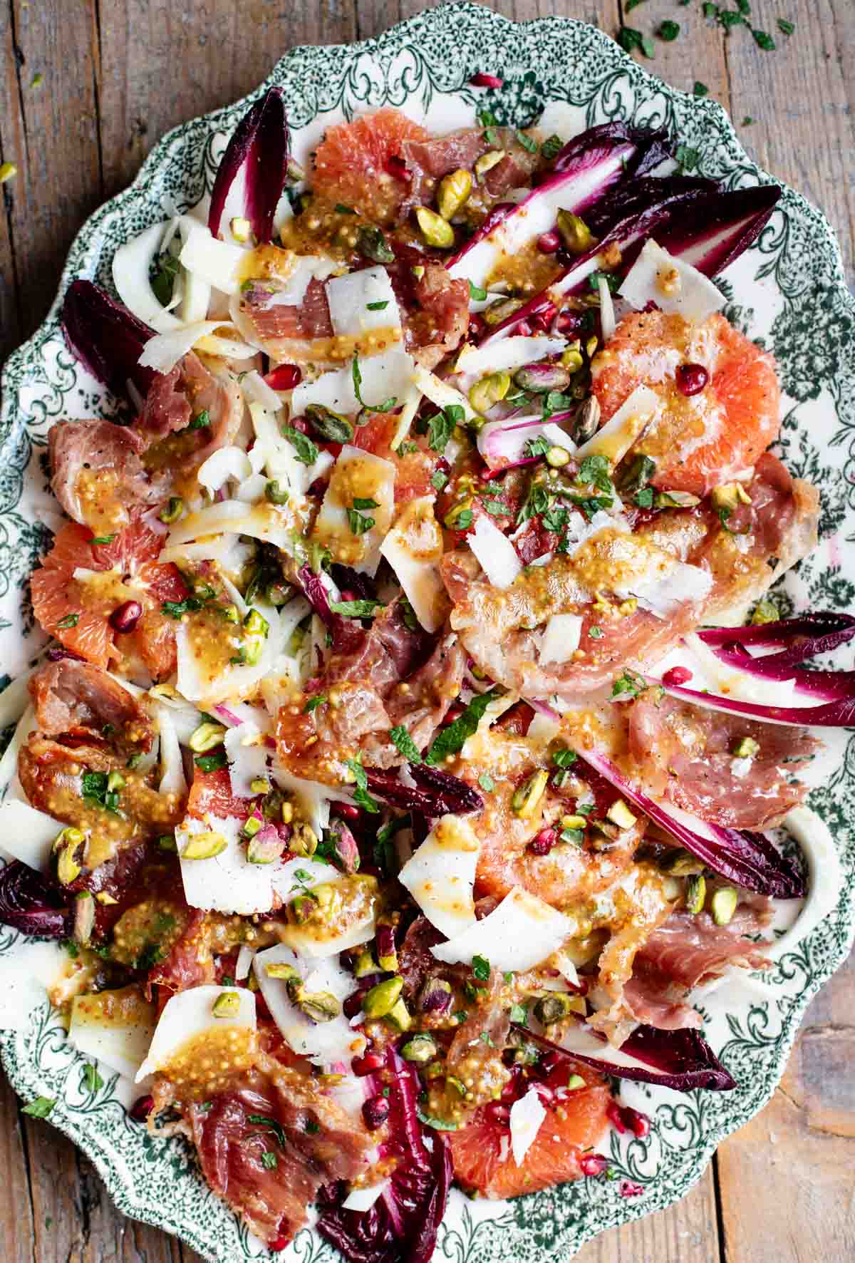 A green serving platter with a festive, colourful salad filled with blood orange, raddichio, fennel, pomegranate, pistachios and prosciutto.