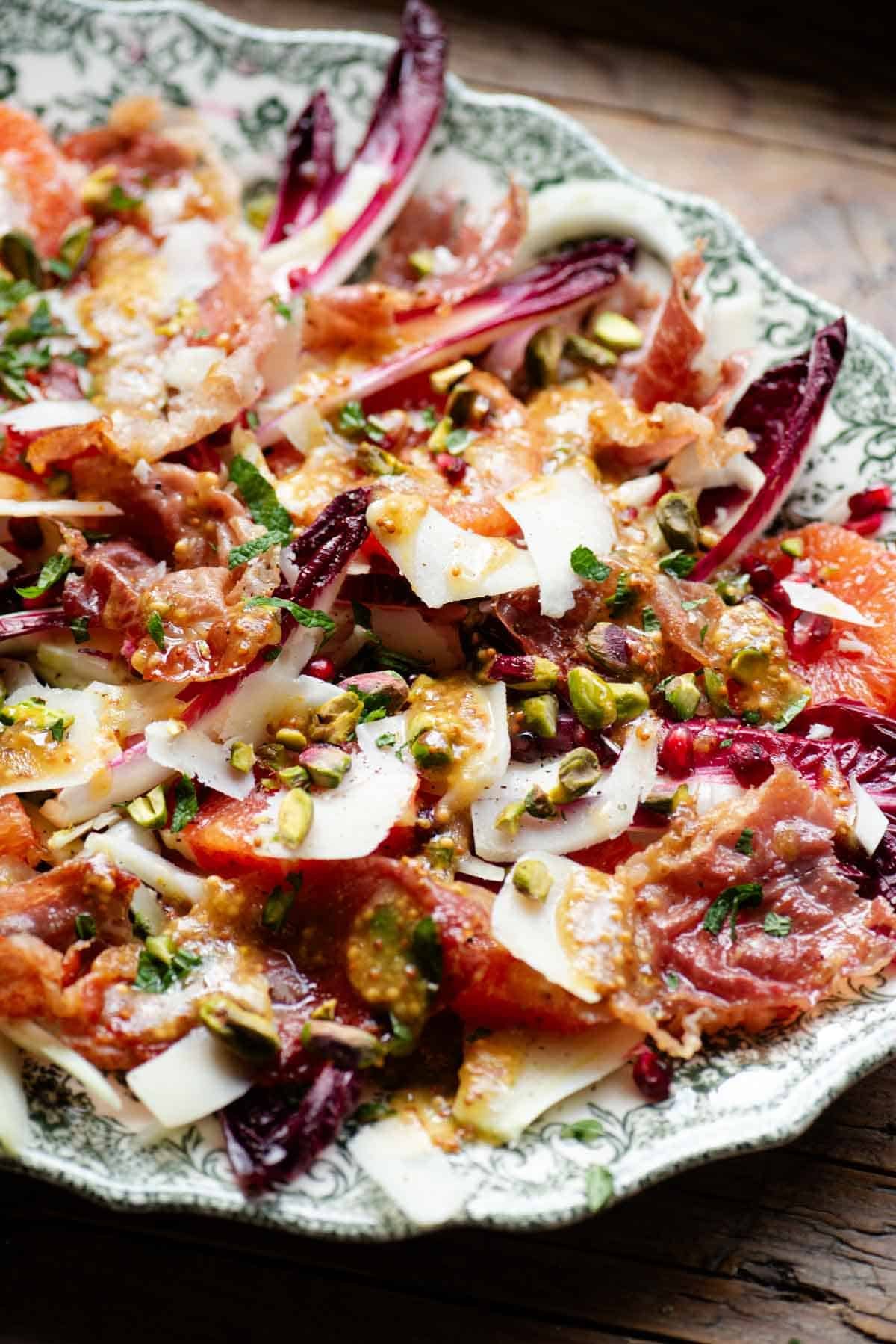 A side shot of a festive salad with blood orange, raddichio, prosciutto, pecorino, pomegranate and pistachios.