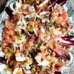 A close up of a festive salad on a serving plate made with blood orange, chicory, fennel, prosciutto, pecorino, pomegranate and pistachios.